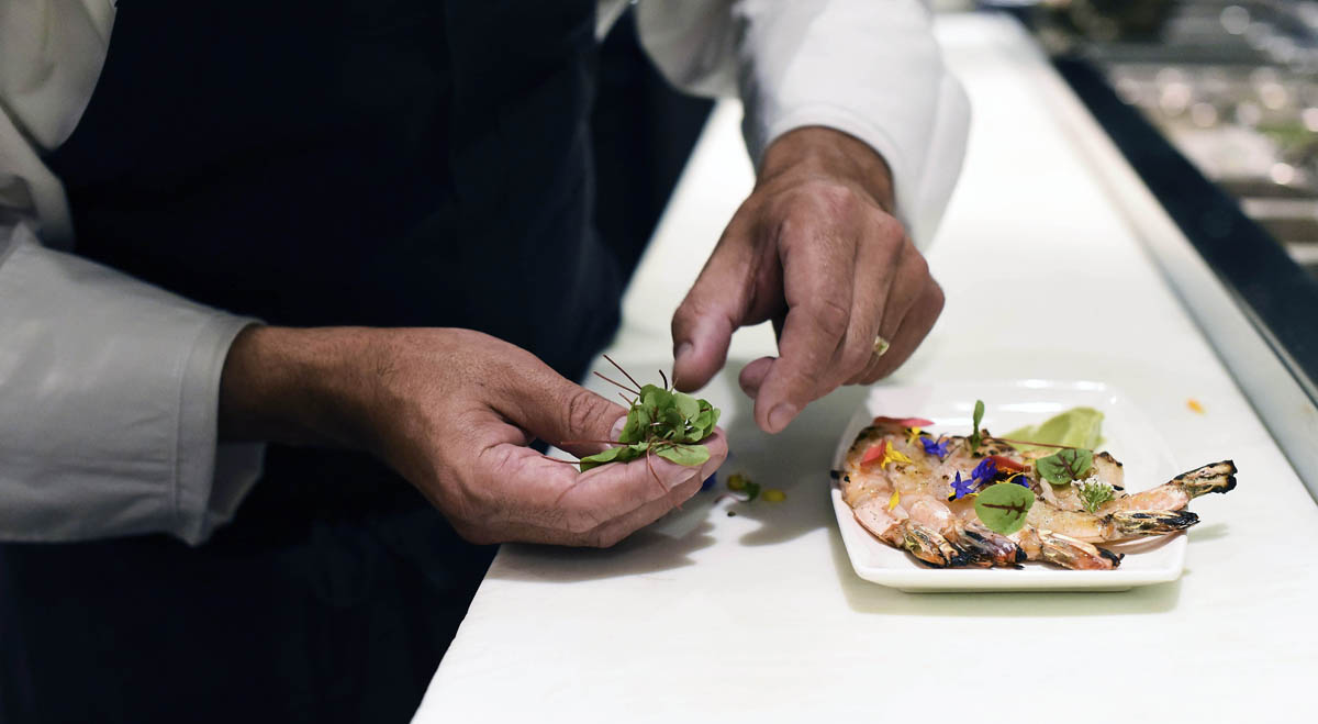 Seared shrimp with edible flowers are carefully arranged on a plate 