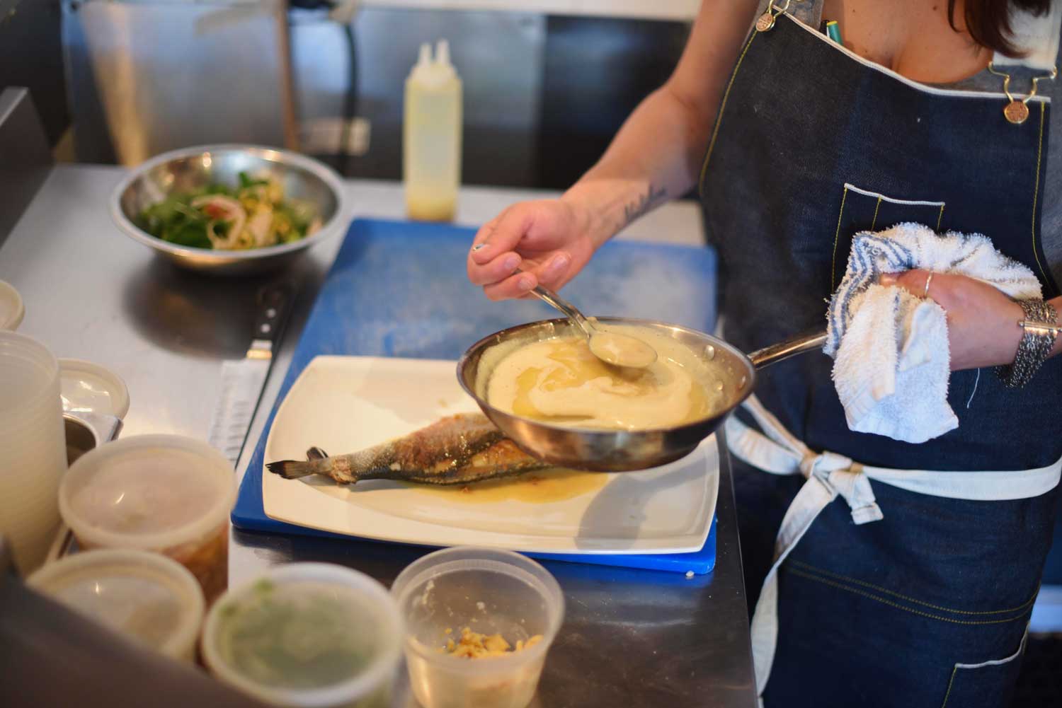Chef Melissa spoons a butter sauce onto the pan seared fish.