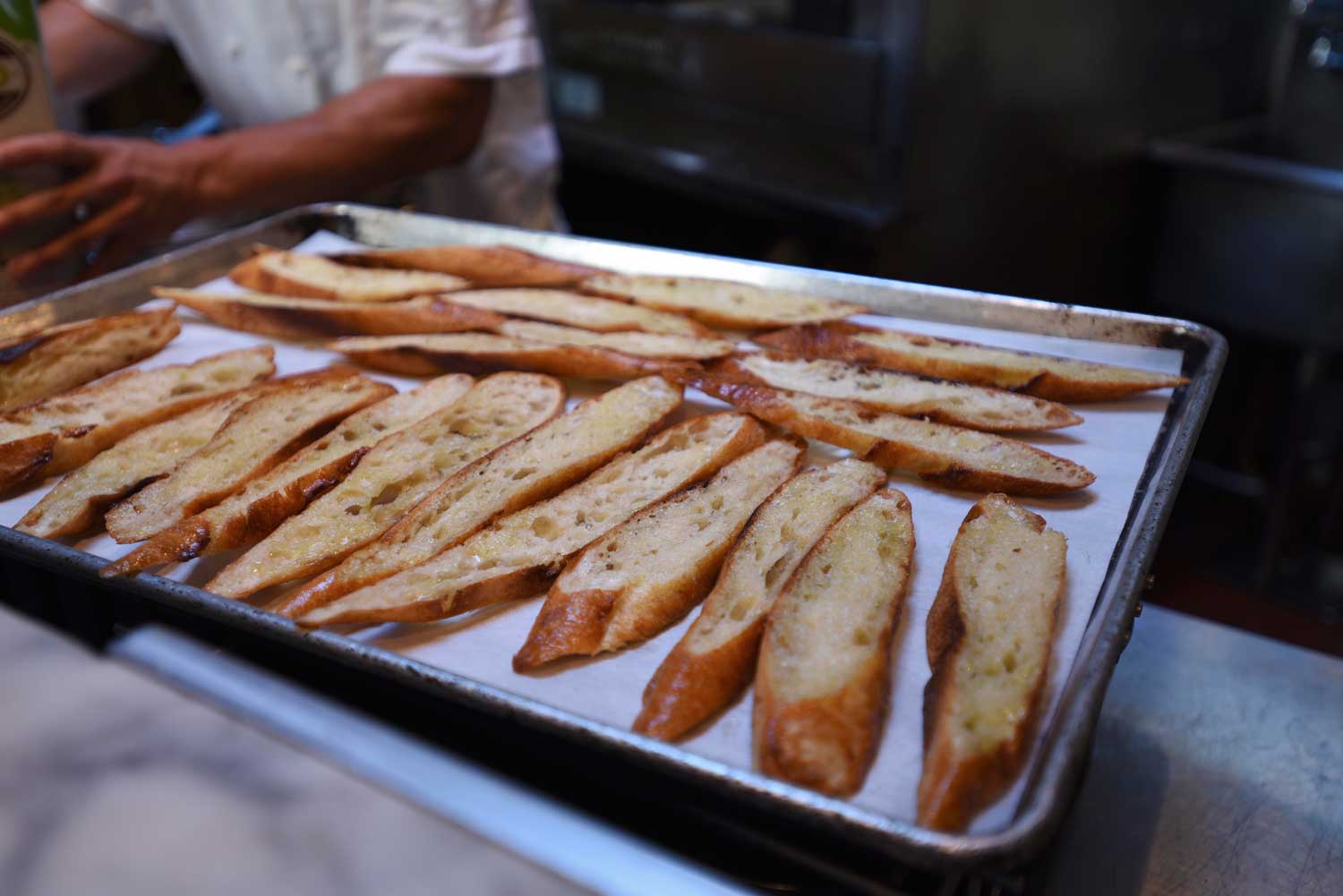 Italian loaves are sliced and drizzled with olive oil in preparation for dinner at Delfina