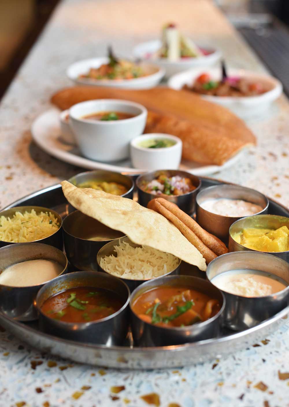 Papadum bread and sides, a dosa, and small plates line the bar at Dosa on Fillmore 