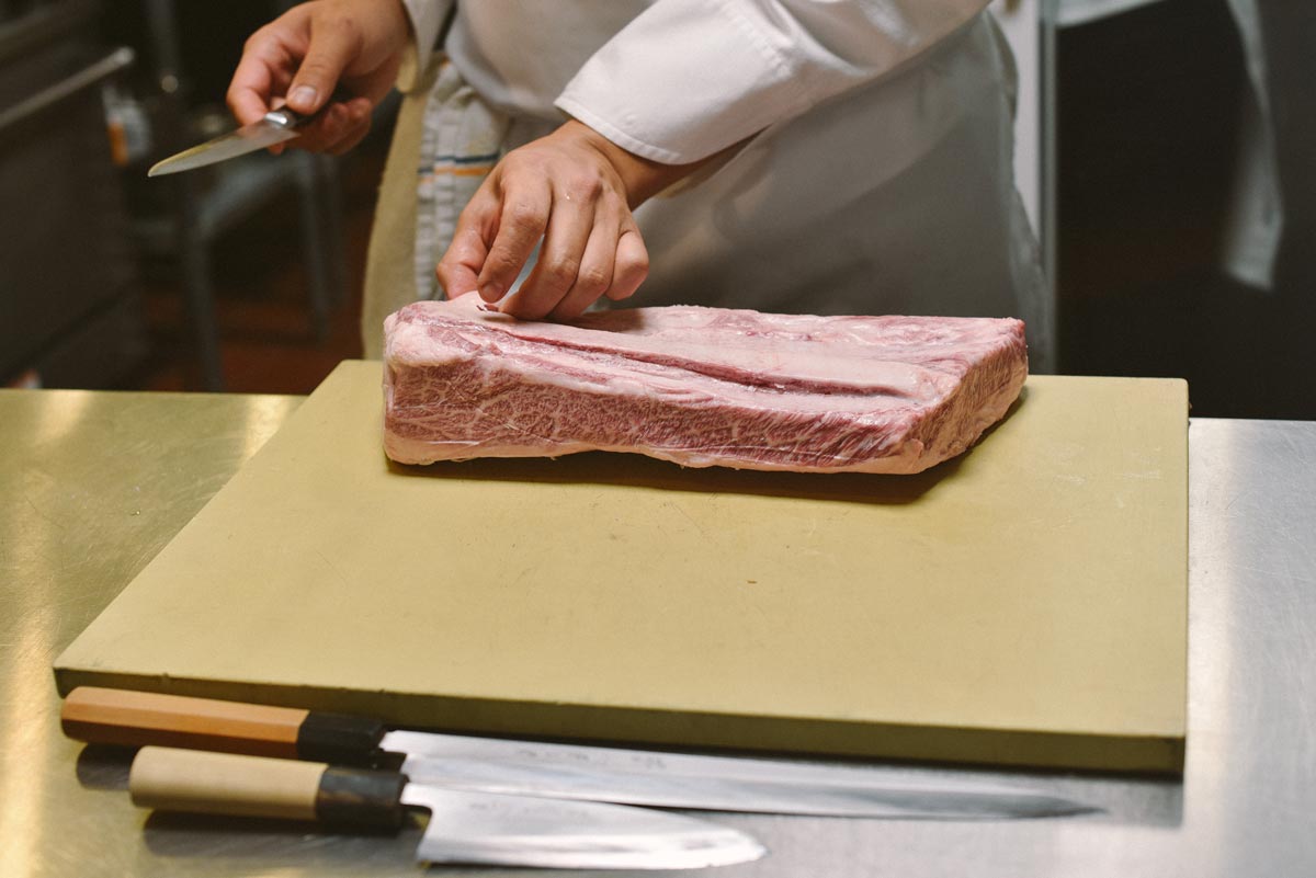 Chef Anh begins to prepare a cut of meat with his knives 