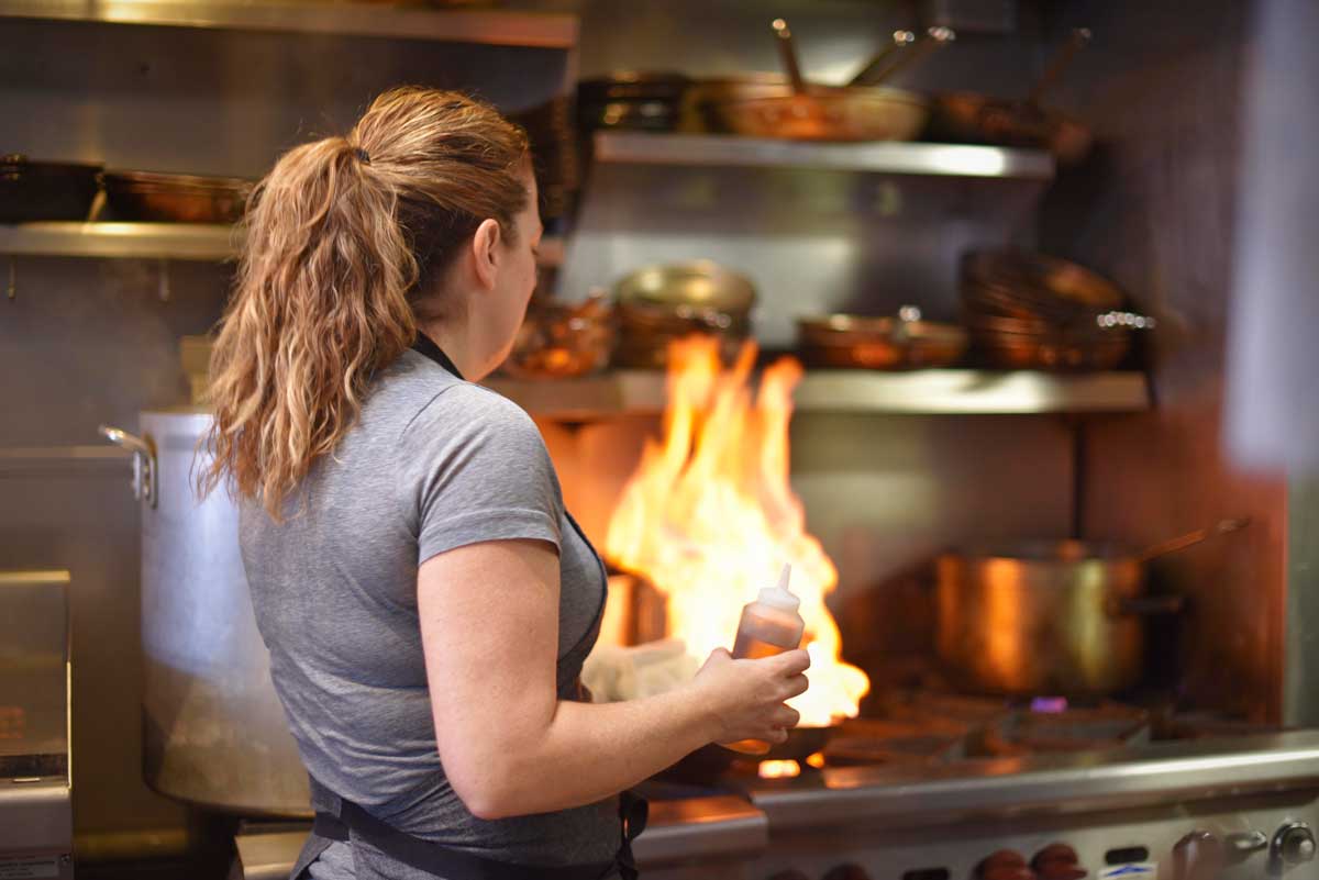 Chef Trish Tracey flames a dish on the stove. 
