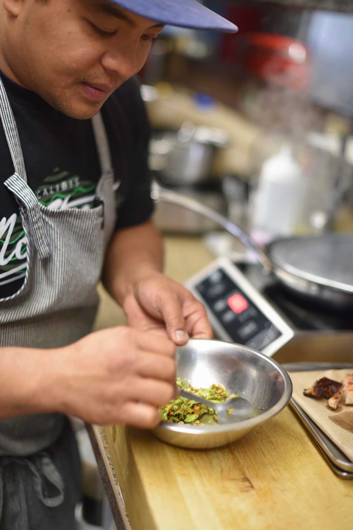 Mixing greens to top the ground chicken neck stuffed banana leaf. 