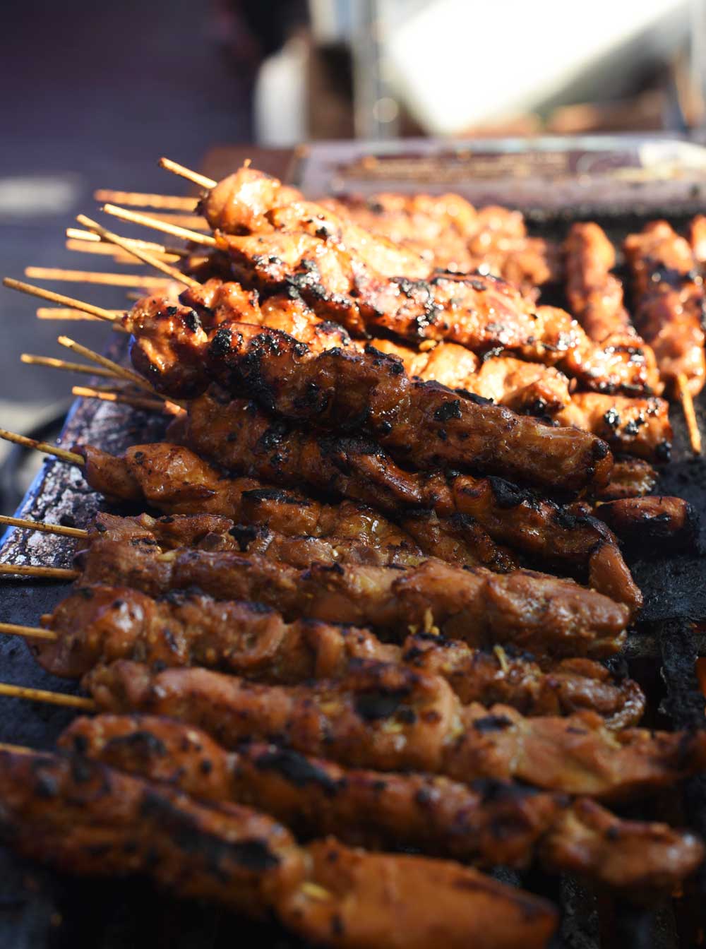 Chicken satays sizzle on an open air grill at the Satasfied food stand at Outside Lands in San Francisco.
