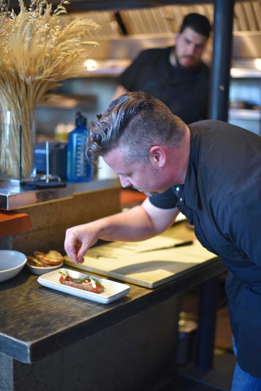 A member of chef Isaac Miller's team watches him carefully preparing a plate  