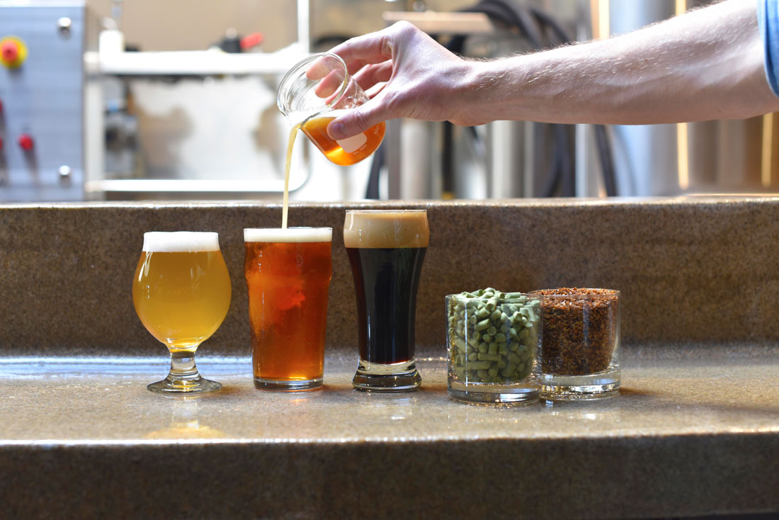The brewmaster pours some more ale from a beaker to top off a pint glass